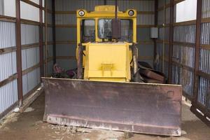 trator de rodas grande com lâmina de trator para limpar estradas da neve. carregadeira de rodas amarela na garagem. foto