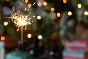 vela de estrelinhas de natal queima no fundo da árvore de natal. decoração de iluminação de natal em casa interior. magia festiva acende luzes para festa natalícia. véspera de natal com fogos de artifício. foto