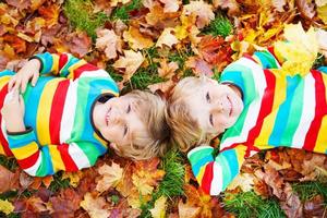 dois meninos deitados em folhas de outono com roupas coloridas