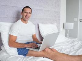 homem feliz usando laptop na cama foto