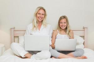 mãe e filha felizes usando laptops na cama foto