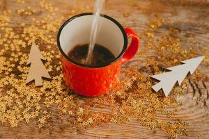 brilhos de ouro e árvores de natal de madeira em um fundo de madeira. fundo de natal feito de brilhos e xícaras vermelhas com café. a água é derramada em um copo. foto