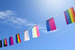 bandeira do arco-íris e bandeiras lgbtq penduradas no fio contra fundo nublado e azul, foco suave e seletivo. foto