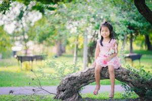 menina asiática com uma boneca sentada no parque foto