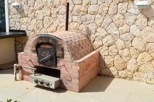 um grande forno de forno de pedra marrom industrial profissional com um tubo para cozinhar alimentos fritos de uma pedra ladrilhada em um fundo de parede de pedra na rua ao ar livre foto