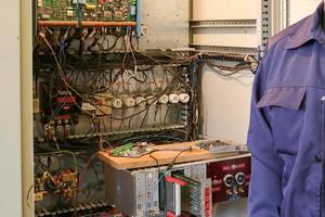 um eletricista de trabalho masculino fica na frente de um painel elétrico com fios, transistores, fusíveis, eletrônicos e interruptores foto