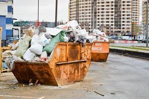 grande lata de lixo industrial de ferro. uma bagunça com lixo com sujeira, falta de segurança, condições insalubres e poluição ambiental em um canteiro de obras industrial foto