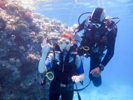 uma linda garota mergulhadora mostra sinal de gesto com as mãos tudo bem com um instrutor parceiro para segurança flutua sob a água no mar vermelho com recifes de corais egito, sharm el-sheikh foto