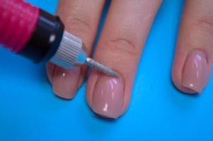 o processo de fazer uma bela manicure nos dedos de um dedo processando uma unha com uma máquina especial em um salão de beleza de unhas em um fundo azul foto