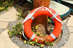 a bóia salva-vidas laranja para a segurança da natação repousa sobre um piso de pedra contra um fundo de flores amarelas e espreguiçadeiras no resort tropical marinho exótico de calor do sul foto