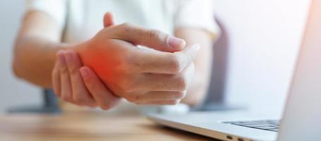 mulher com dor no pulso ao usar computador portátil e mouse durante muito tempo de trabalho no local de trabalho. tenossinovite de quervain, reumatismo ergonômico, síndrome do túnel do carpo ou conceito de síndrome do escritório foto