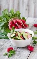 salada fresca de pepinos e rabanetes em uma tigela branca sobre o antigo fundo de madeira foto