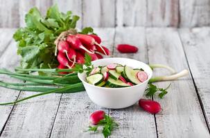 salada fresca de pepinos e rabanetes em uma tigela branca sobre o antigo fundo de madeira foto