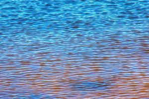 fundo de textura de ondulação de água. superfície da água ondulada durante o pôr do sol, luz dourada refletindo na água. foto