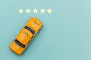 táxi de carro de brinquedo amarelo e classificação de 5 estrelas isolada em fundo azul. aplicativo para smartphone do serviço de táxi para pesquisa on-line chamando e reservando o conceito de táxi. símbolo de táxi. copie o espaço. foto