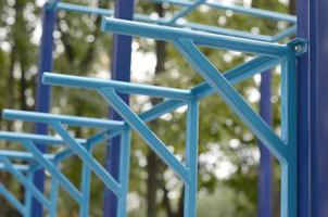 tubos de metal azul e barras transversais contra um campo de esportes de rua para treinamento de atletismo. equipamento de ginástica esportiva ao ar livre. foto macro com foco seletivo e fundo extremamente desfocado