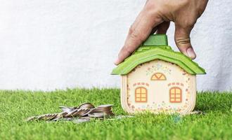 maquete de casa com pilha de moedas no chão de grama e mão colocando maquete de casa. foto