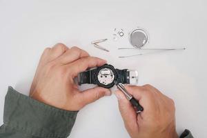 um homem usa um alicate para prender a bateria do relógio digital, remover e trocar na reparação de relógios de pulso quebrados na mesa branca foto