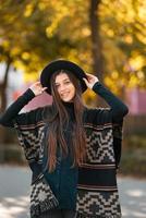 mulher elegante de poncho e chapéu gosta de parque de outono foto