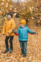 meninos em uma jaqueta espalham folhas em um parque de outono. a criança se alegra com as folhas de outono. os meninos estão felizes com o outono. caminhando no parque outono. Infância feliz