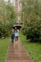 mãe com uma jaqueta azul caminha no parque com seu filho ao longo de um caminho de madeira com um guarda-chuva foto