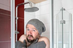 homem de chapéu e luvas no chuveiro sob água fria. conceito de crise de energia e economia. foto