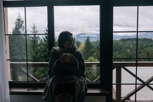 silhueta de uma mulher sentada no peitoril da janela com uma caneca foto