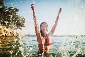 mulher espirrando na água do mar e se divertindo nas férias de verão foto