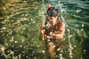 mulher com máscara de mergulho espirrando na água do mar e se divertindo nas férias de verão foto