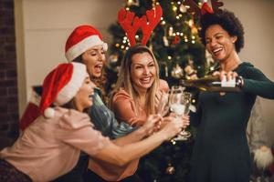 quatro mulheres multiétnicas se divertindo e fazendo torradas enquanto comemoram em casa a festa de natal foto