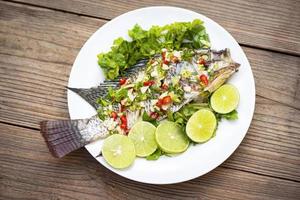 peixe tilápia cozido no vapor com molho de pimenta e limão com ervas e vegetais no prato, peixe com limão - comida tailandesa foto