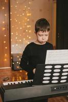 um menino em uma camiseta preta toca piano, no contexto de uma guirlanda de natal foto