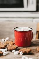 copo vermelho com close-up de cacau e marshmallows em um fundo de madeira. biscoitos de natal e outros doces com cacau