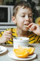 menino toma café da manhã com cereais com leite. café da manhã na cozinha antes da escola. o menino está comendo na mesa perto da janela. foto