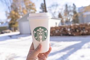 marinette, wi, eua - 14 de novembro de 2019- xícaras de café quente starbucks colocadas na neve branca no jardim de inverno, bebida fresca e quente para levar o conceito. starbucks cafe coffee shop. foto