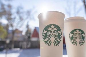 marinette, wi, eua - 14 de novembro de 2019- xícaras de café quente starbucks colocadas na neve branca no jardim de inverno, bebida fresca e quente para levar o conceito. starbucks cafe coffee shop. foto