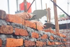 trabalhadores da construção civil instalam tijolos e cimento de fileiras de tijolos nas paredes externas foto