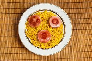 arroz amarelo em um prato com linguiça frita. foto