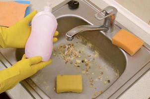limpador mostra garrafa de detergente líquido de limpeza na pia da cozinha suja com partículas de alimentos antes da limpeza foto