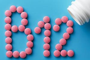 pílulas cor de rosa na forma da letra b12 em um fundo azul, derramadas de uma lata branca. foto