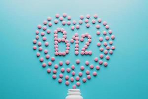 comprimidos rosa na forma de b12 no coração em um fundo azul, derramado de uma lata branca de baixo contraste foto