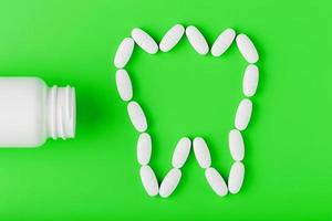 vitamina de cálcio na forma de um dente derramado de uma jarra branca sobre um fundo verde. foto