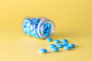 frasco de medicamento e comprimidos azuis derramados sobre fundo amarelo. foto