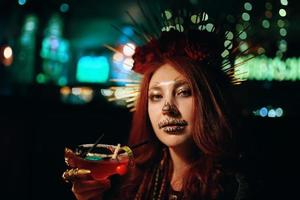 mulher com maquiagem de esqueleto em uma festa de halloween detém coquetel. foto