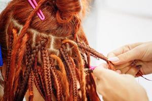 mãos de cabeleireiro trançam dreadlocks ruivos de menina. foto