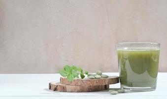 bebida saudável de spirulina no copo com comprimidos de spirulina chlorella no pódio de corte de serra de árvore. superalimento, bebida desintoxicante. cuidados de saúde, bebida antioxidante. copie o espaço foto