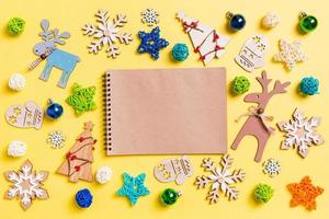 vista superior do notebook em fundo amarelo com brinquedos e decorações de ano novo. conceito de tempo de natal foto