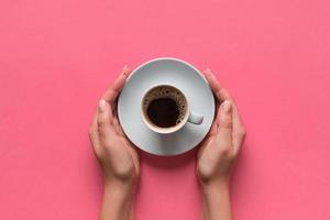 alto ângulo de mãos de mulher segurando uma xícara de café no estilo minimalista de fundo rosa. configuração plana, vista superior isolada foto