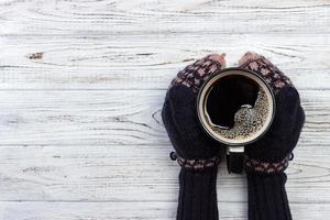 mãos femininas em luvas segurando uma xícara de café em fundo de madeira foto