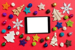 vista superior do tablet digital sobre fundo vermelho feito de brinquedos e decorações do feriado. conceito de enfeite de natal foto